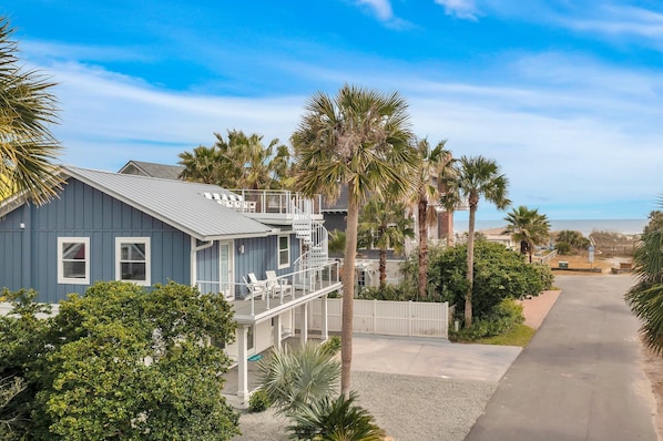 A coastal house with a balcony, palm trees, and a clear sky.