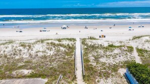Una spiaggia con un sentiero sabbioso che conduce all'acqua, ombrelloni e bagnanti.