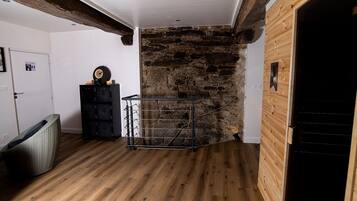 Una habitación con pared de piedra, vigas de madera, un perchero metálico y una puerta.