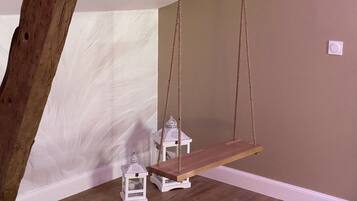 A wooden swing suspended from the ceiling in a room with white walls and a wooden floor.