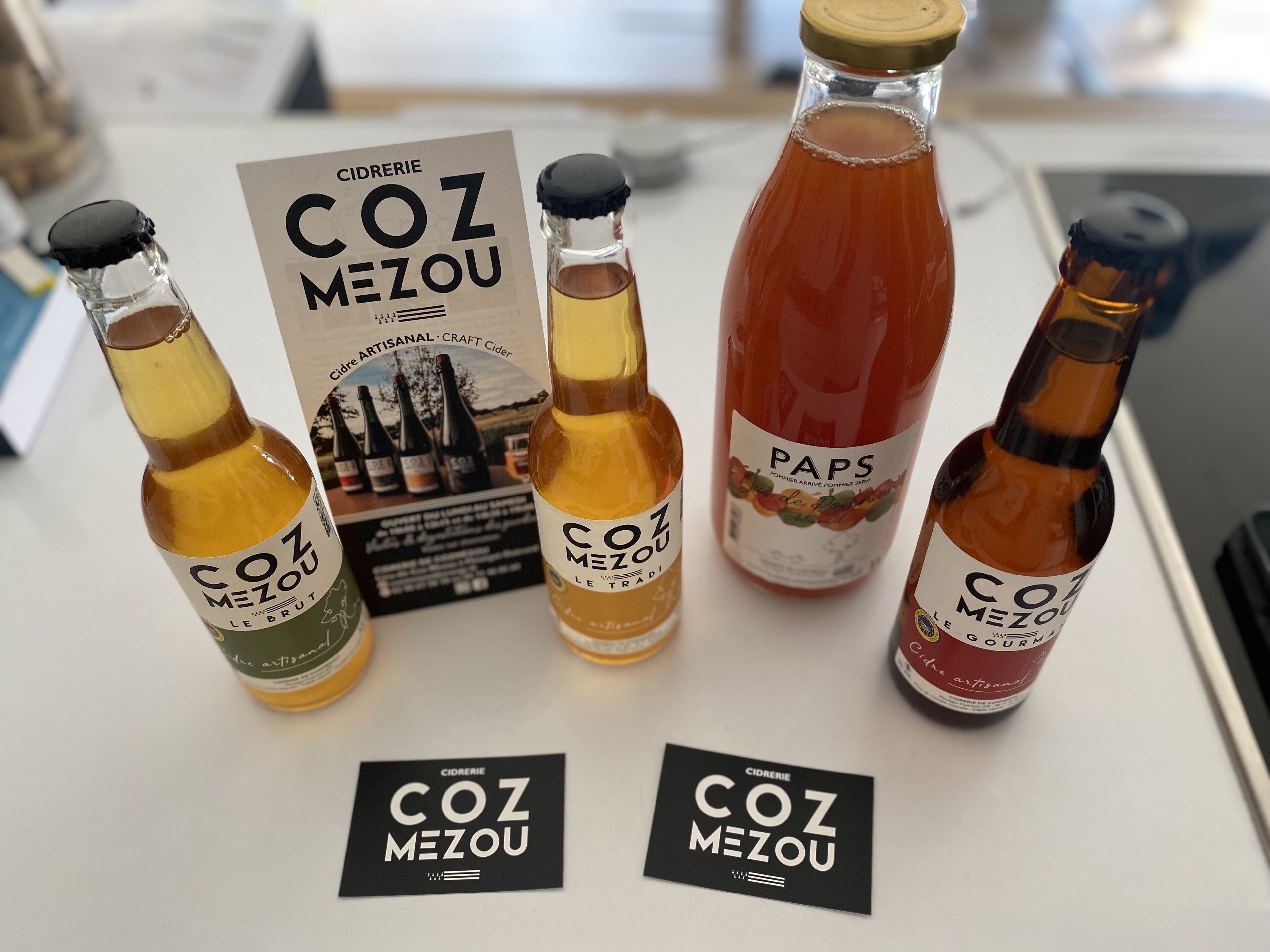 Four bottles of cider and two business cards on a table.