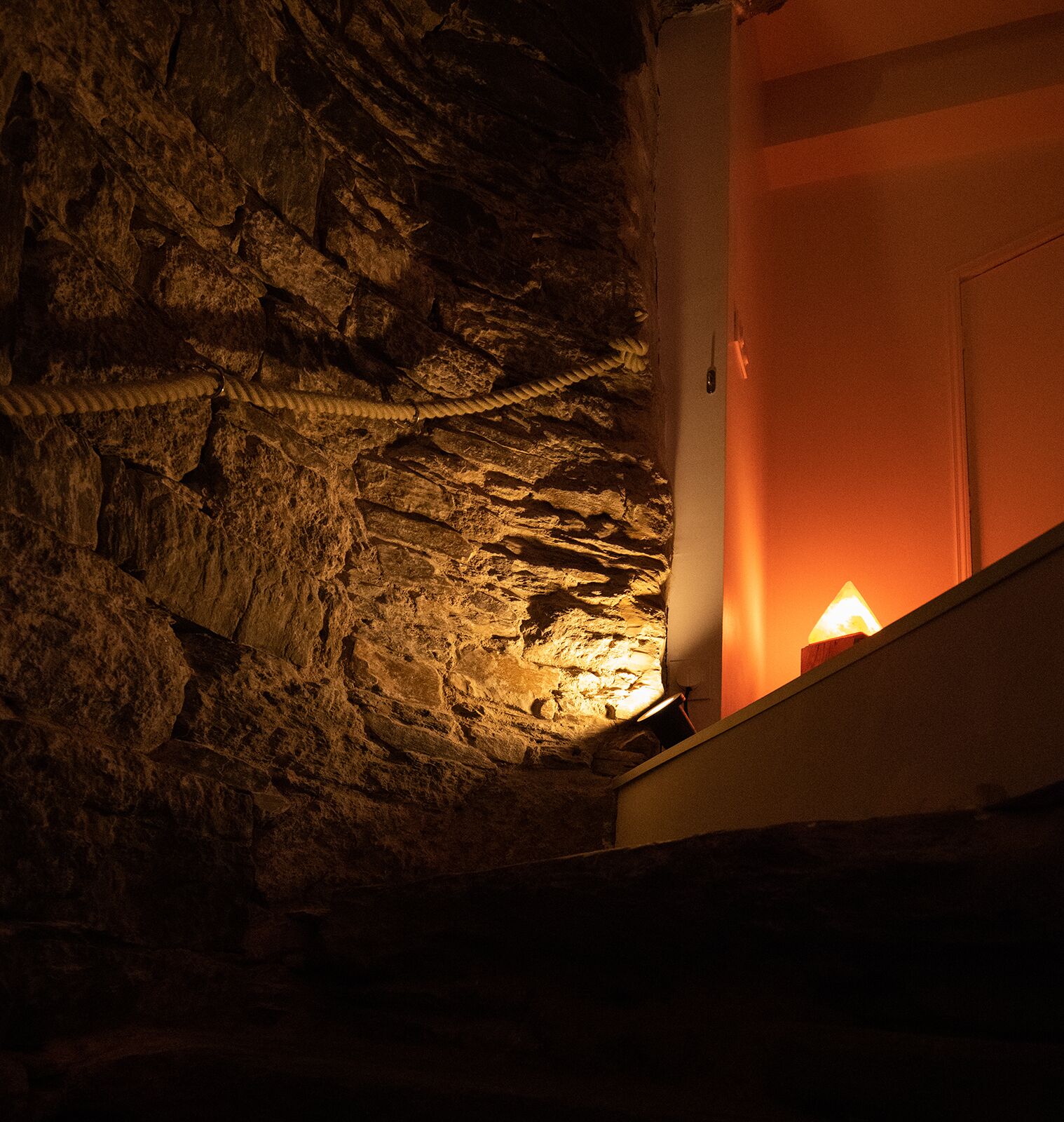 A dimly lit room with a rough, textured wall and a rope coiled on it.