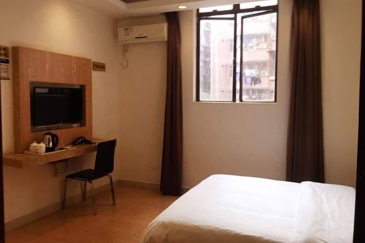 A hotel room with a bed, a desk with a chair, a television, and a window with curtains.