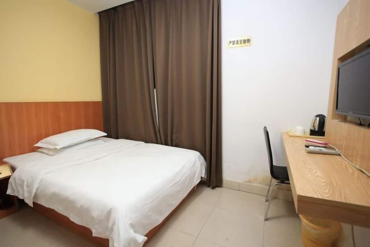 A hotel room with a bed, a desk with a chair, a television, and a sign on the wall.