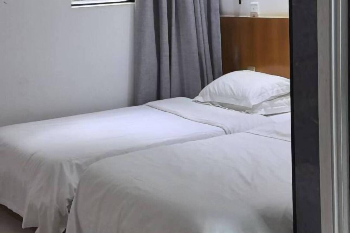 A single bed with white bedding, a grey curtain, and a wooden headboard.