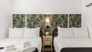 A hotel room with two beds, a nightstand, and a wall with a leafy pattern. - Marsh Hotel (New Orleans)