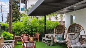 A patio with artificial grass, wicker furniture, and a covered area with a pergola. - Marsh Hotel (New Orleans)