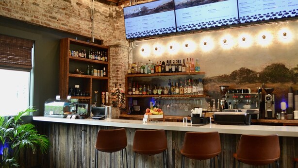 A bar area with a menu board, shelves of liquor bottles, and bar stools. - Marsh Hotel (New Orleans)