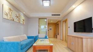 A modern living room with a blue sofa, a wooden coffee table, and a flat-screen TV mounted on the wall. - Tuke China Light Residence Hotel (Shiyan Wudangshan Airport Branch) (Shiyan)