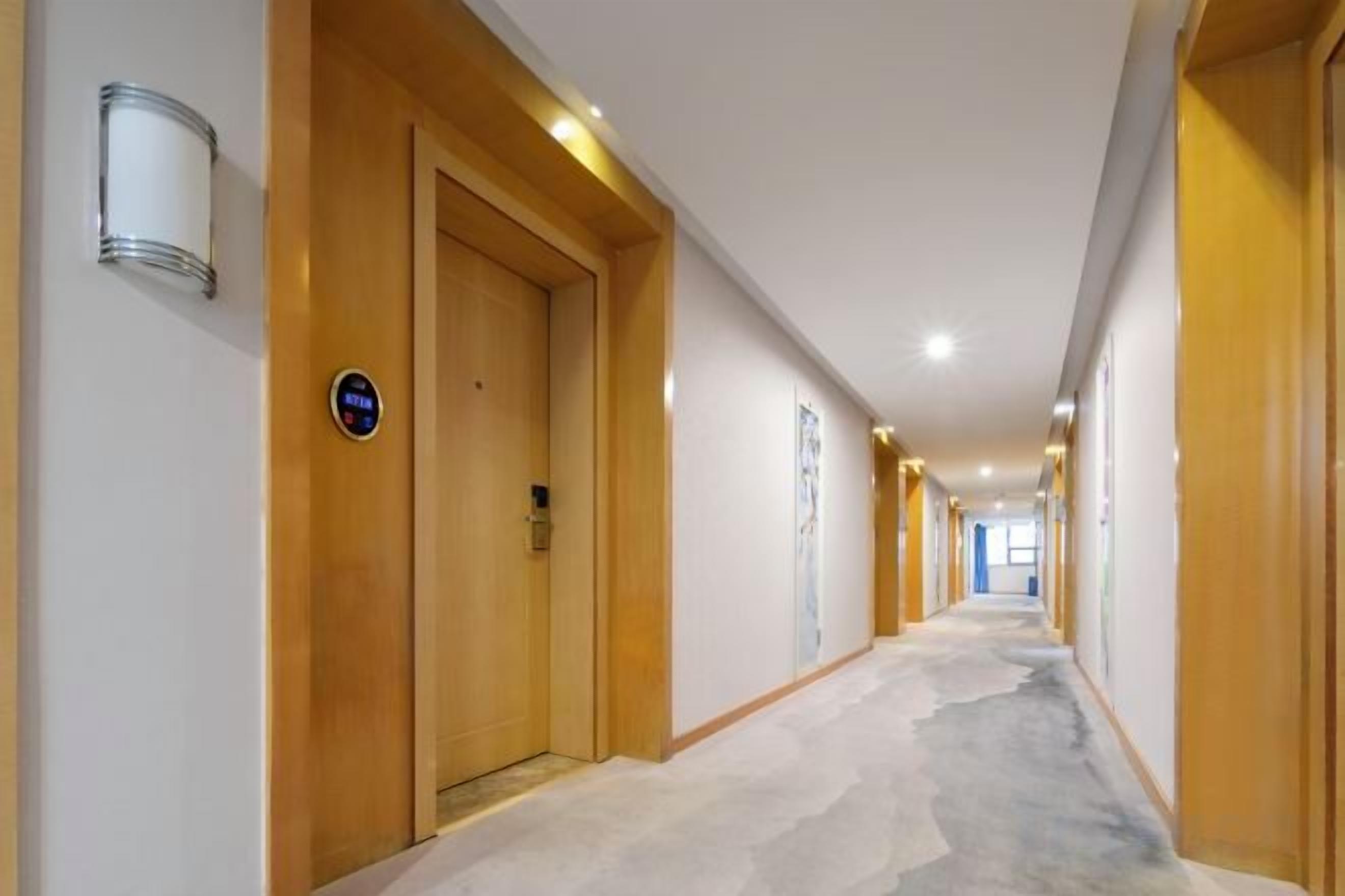 A hotel corridor with wooden doors, a carpeted floor, and a light fixture on the wall.