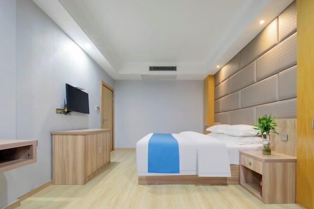 A hotel room with a bed, bedside tables, a TV mounted on the wall, and a wooden cabinet.