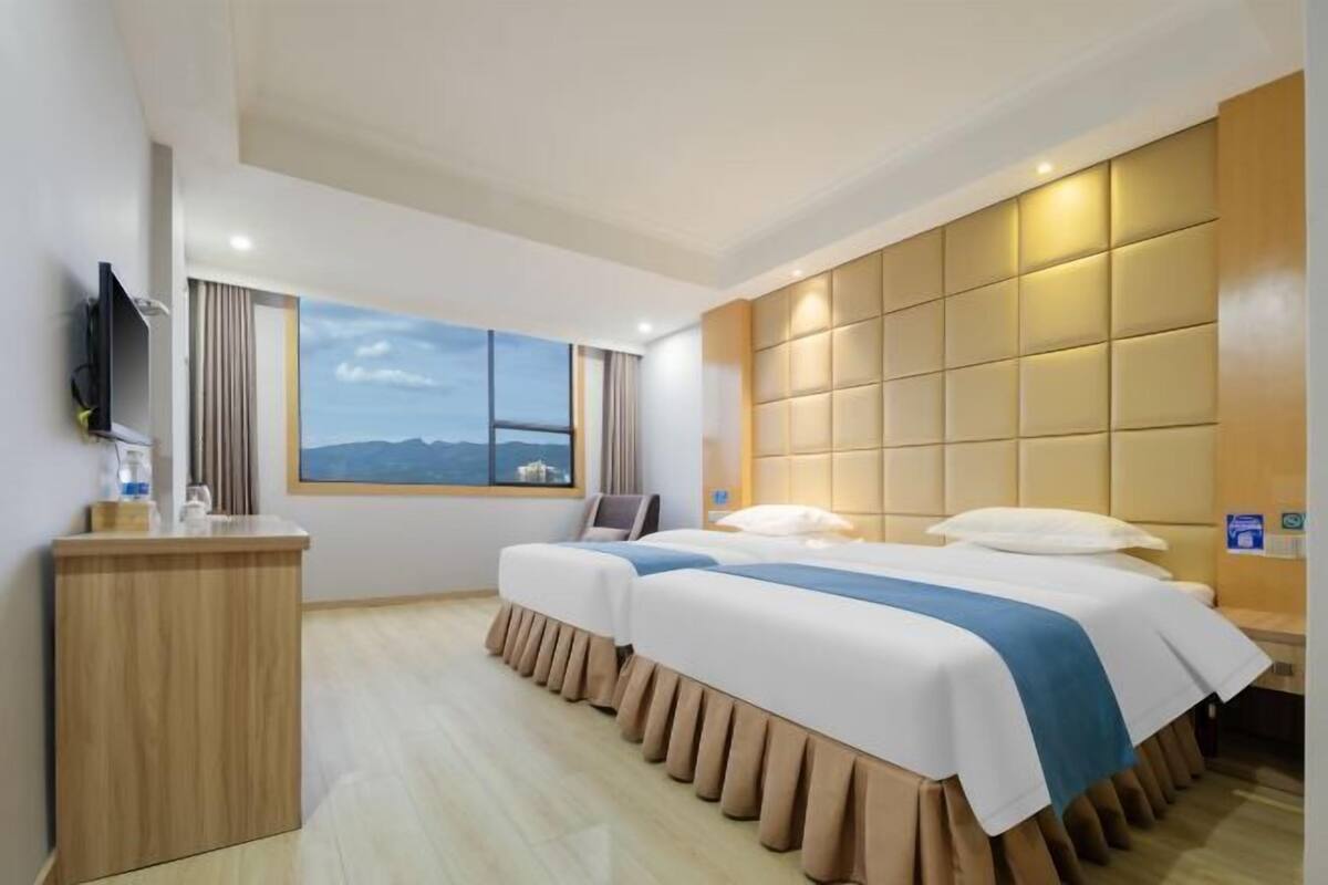 A hotel room with a large bed, a wooden desk, a TV, and a window with a mountain view.