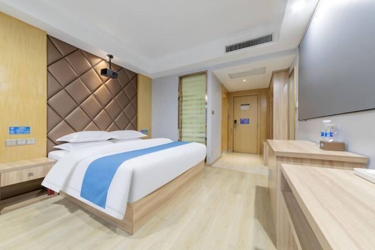 A hotel room with a bed, bedside tables, a flat-screen TV, and a wooden headboard.