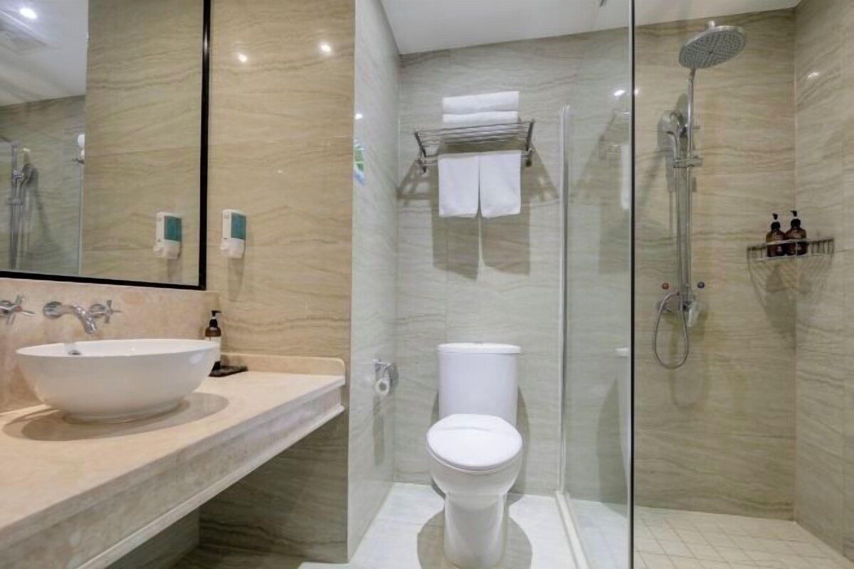 A modern bathroom with a large white sink, a toilet, and a glass-enclosed shower area.