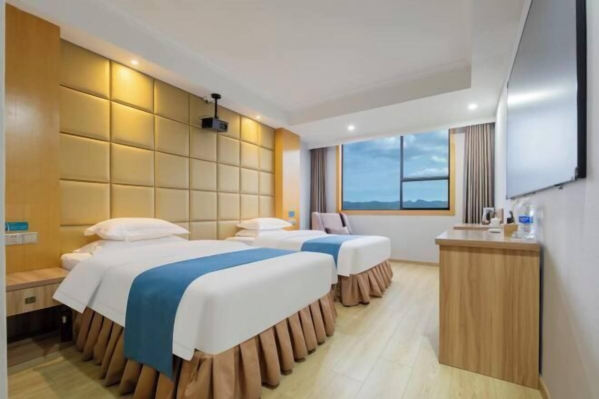 A hotel room with two beds, a desk, a TV, and a window with a view.