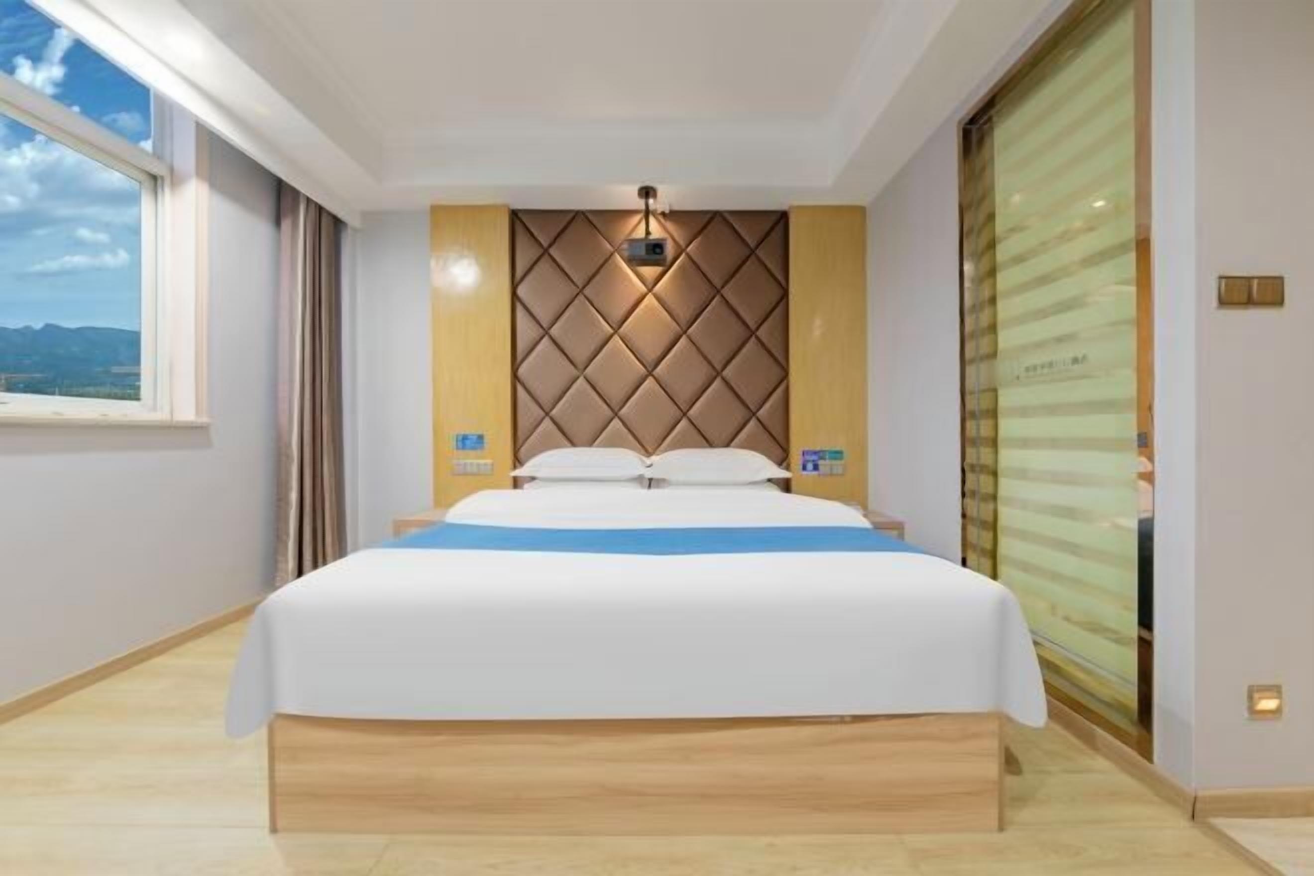 Ein Hotelzimmer mit Bett, Fenster, einem fest installierten Projektor und Blick ins Freie.