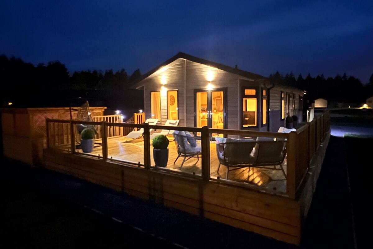 A wooden cabin with a deck, outdoor seating, and a small garden.