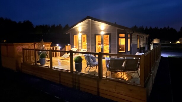 A wooden cabin with a deck, outdoor seating, and a small garden.
