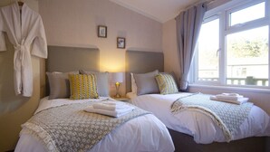 A hotel room with two beds, a robe hanging on the wall, and a window with curtains.