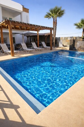 A swimming pool with clear blue water, surrounded by lounge chairs and palm trees.