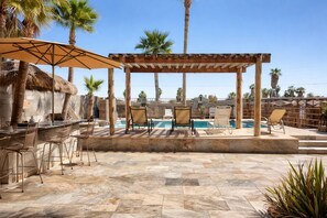 Un espace aménagé au bord de la piscine, comprenant une pergola, des chaises longues et un bar.