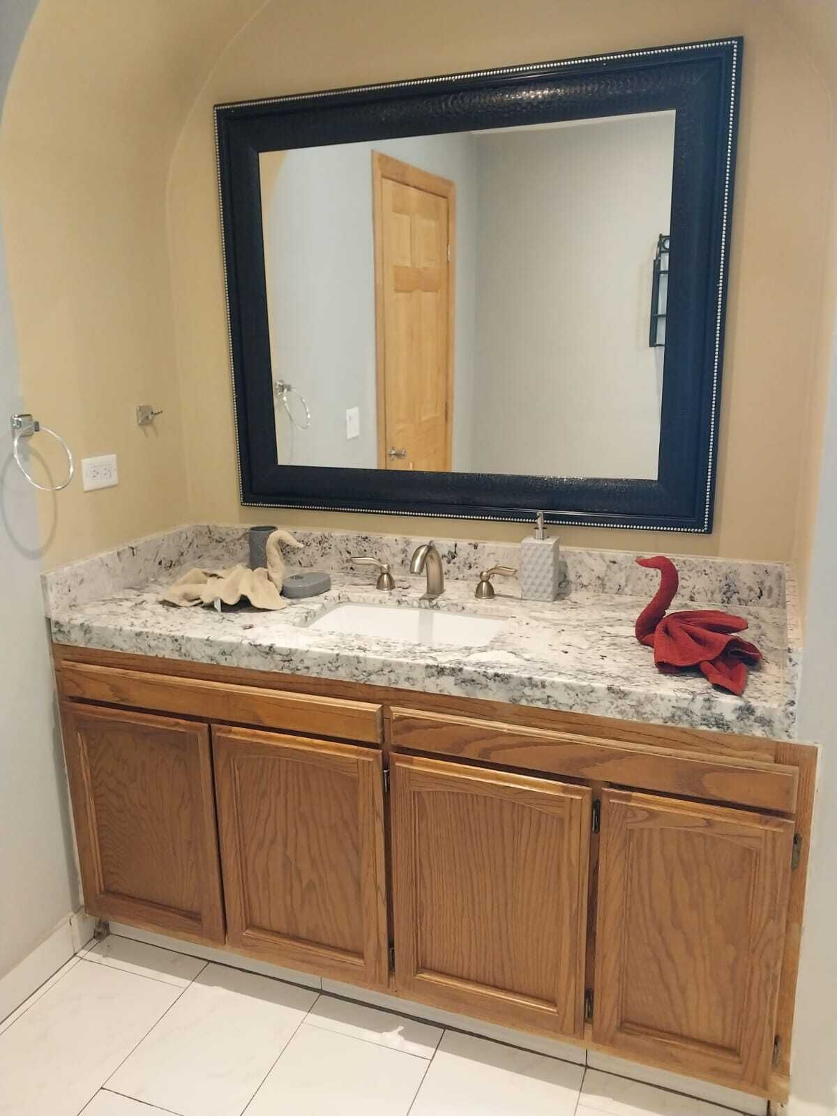 A bathroom with a marble countertop, a sink, a mirror, and wooden cabinets.