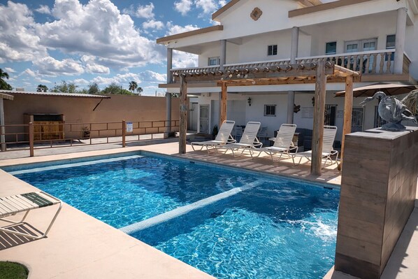 A swimming pool with lounge chairs, a pergola, and a building with balconies.