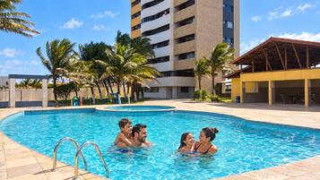 A swimming pool with a clear blue water surface, surrounded by palm trees and a tall building in the background.