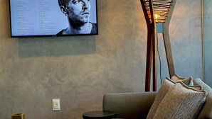 A modern living room with a large flat-screen TV displaying a music album cover, a stylish floor lamp, and a comfortable sofa. - Cobertura vista mar com deck privativo (Fortaleza)
