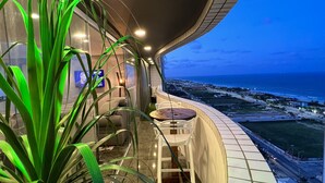 A modern interior with a curved ceiling, a seating area with a table and chairs, and a view of the ocean. - Cobertura vista mar com deck privativo (Fortaleza)
