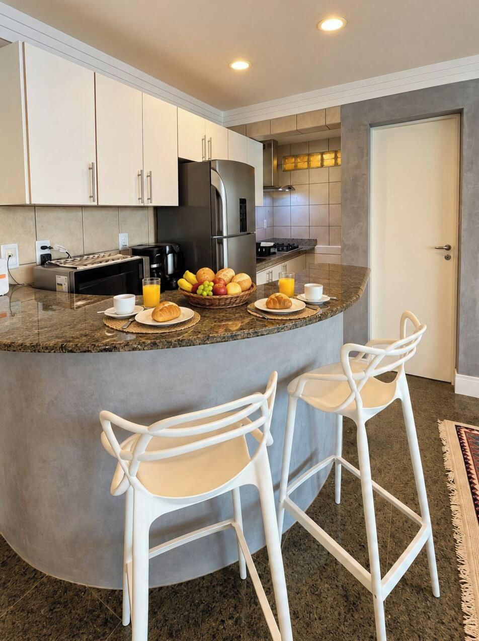 Una cocina moderna con barra desayunadora, armarios blancos y un refrigerador de acero inoxidable.
