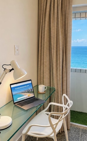 A laptop on a glass table with a white chair, a white mug, and a curtain blocking a view of the sea. - Cobertura vista mar com deck privativo (Fortaleza)