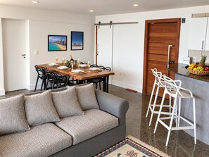 A modern living space with a dining area, a sofa, a kitchen bar, and a sliding door. - Cobertura vista mar com deck privativo (Fortaleza)