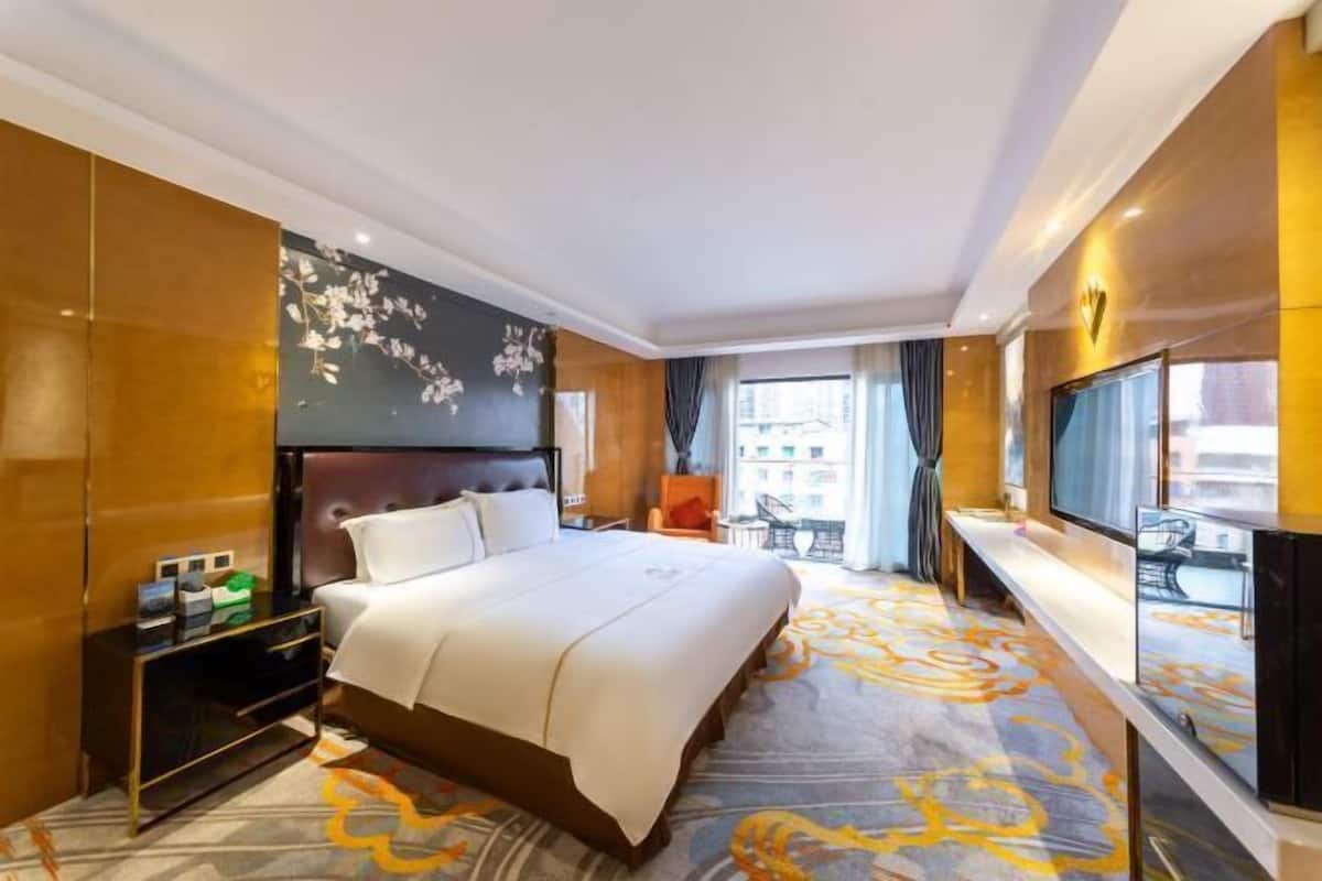A hotel room with a large bed, a TV, a desk, and a view of the city.