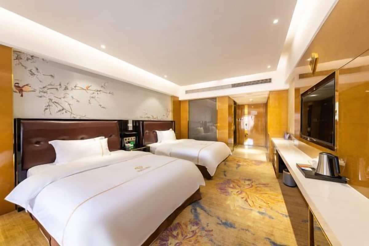 A hotel room with two beds, a TV, and a desk.