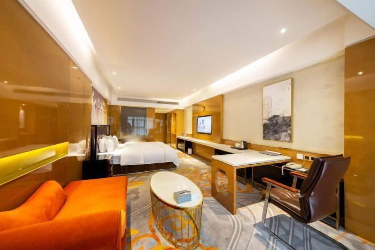 A hotel room with a bed, a desk, a chair, a sofa, and a TV.