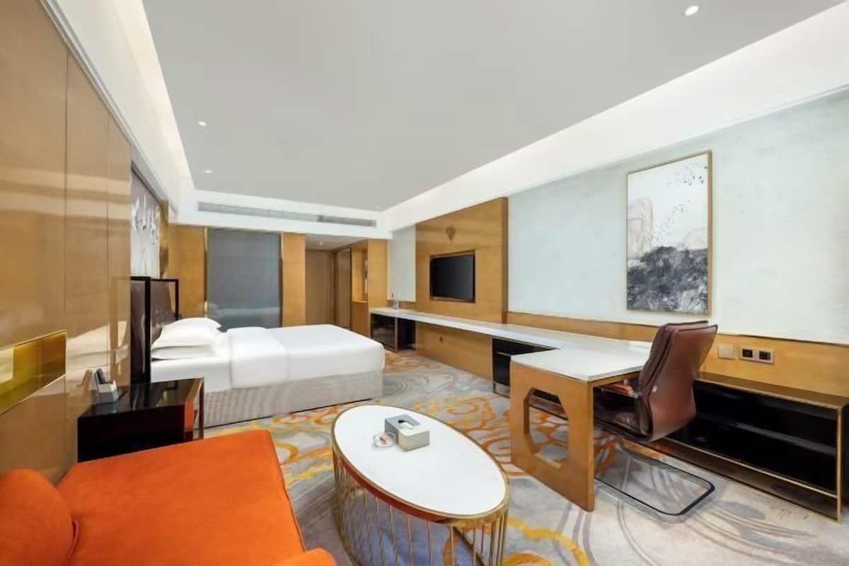 A modern hotel room with a bed, a desk, a chair, and a small table.