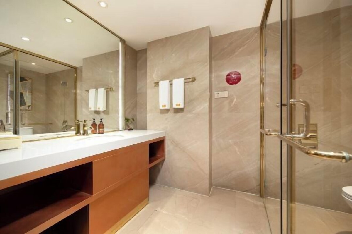 A modern bathroom with a large mirror, a glass shower enclosure, and a white sink with a wooden vanity.