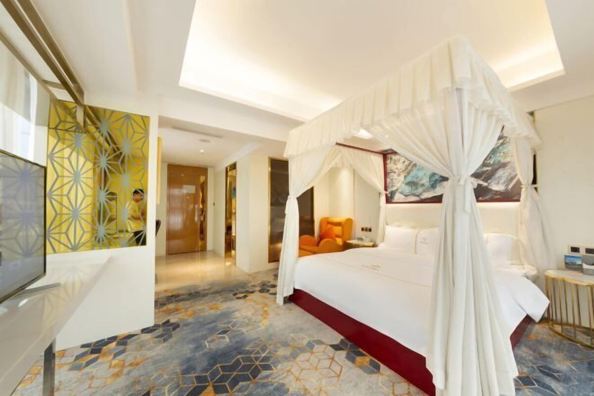 A hotel room with a four-poster bed, a large painting on the wall, and a geometric patterned floor.
