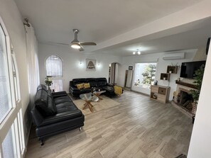 A spacious living room with a black leather sofa, a glass coffee table, and a fireplace.