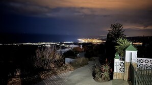 Une vue nocturne d’une ville côtière, avec un pont imposant, une entrée fermée par un portail et un petit bâtiment, ainsi qu’un chemin menant au portail.