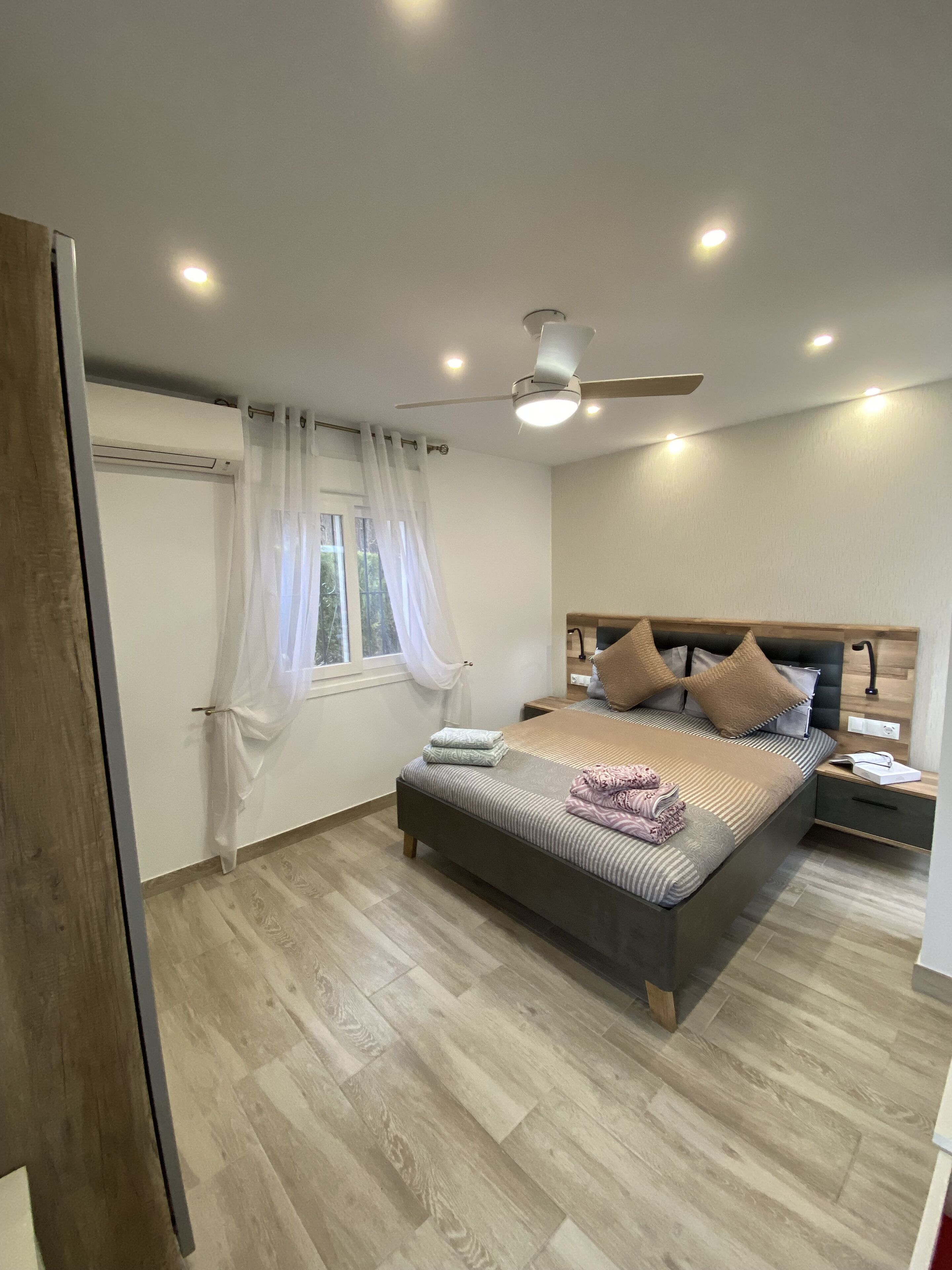 Une chambre à coucher avec un lit, des tables de chevet, un ventilateur de plafond et une fenêtre avec des rideaux.