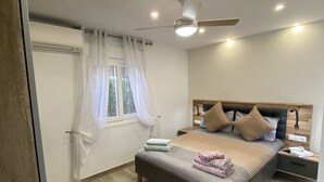 Une chambre à coucher avec un lit, des tables de chevet, un ventilateur de plafond et une fenêtre avec des rideaux.