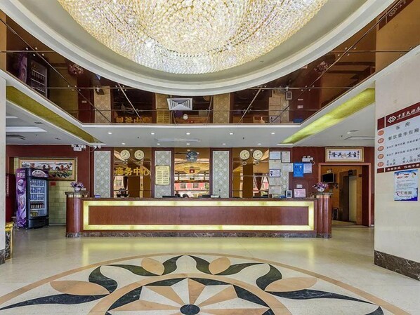 Un hall d’hôtel avec un comptoir d’accueil, un lustre et un sol à motifs.
