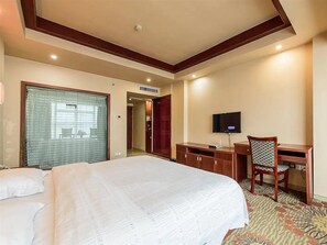 Une chambre d’hôtel avec un grand lit, un bureau avec une chaise, une télévision et une fenêtre avec des rideaux.