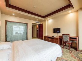 Una habitación de hotel con una cama grande, un escritorio con silla, un televisor y una ventana con cortinas.