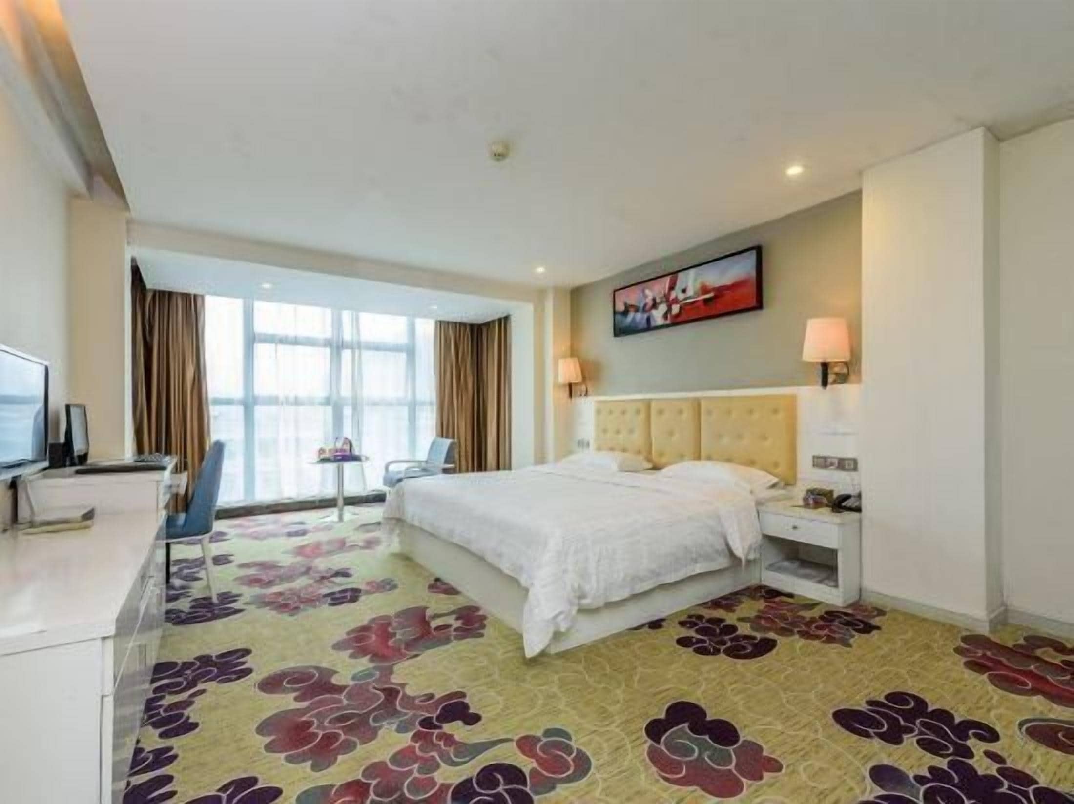 A hotel room with a bed, bedside table, lamp, and a large window.