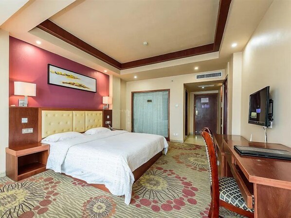 A hotel room with a large bed, a desk, a chair, a television, and a door leading to another room.