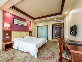 Habitación de hotel con una cama grande, un escritorio, una silla, un televisor y una puerta que da a otra habitación.