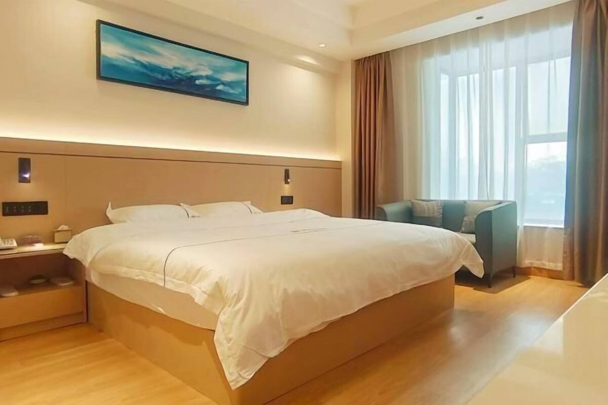 Hotelkamer met een groot bed, nachtkastje, stoel en raam met gordijnen.